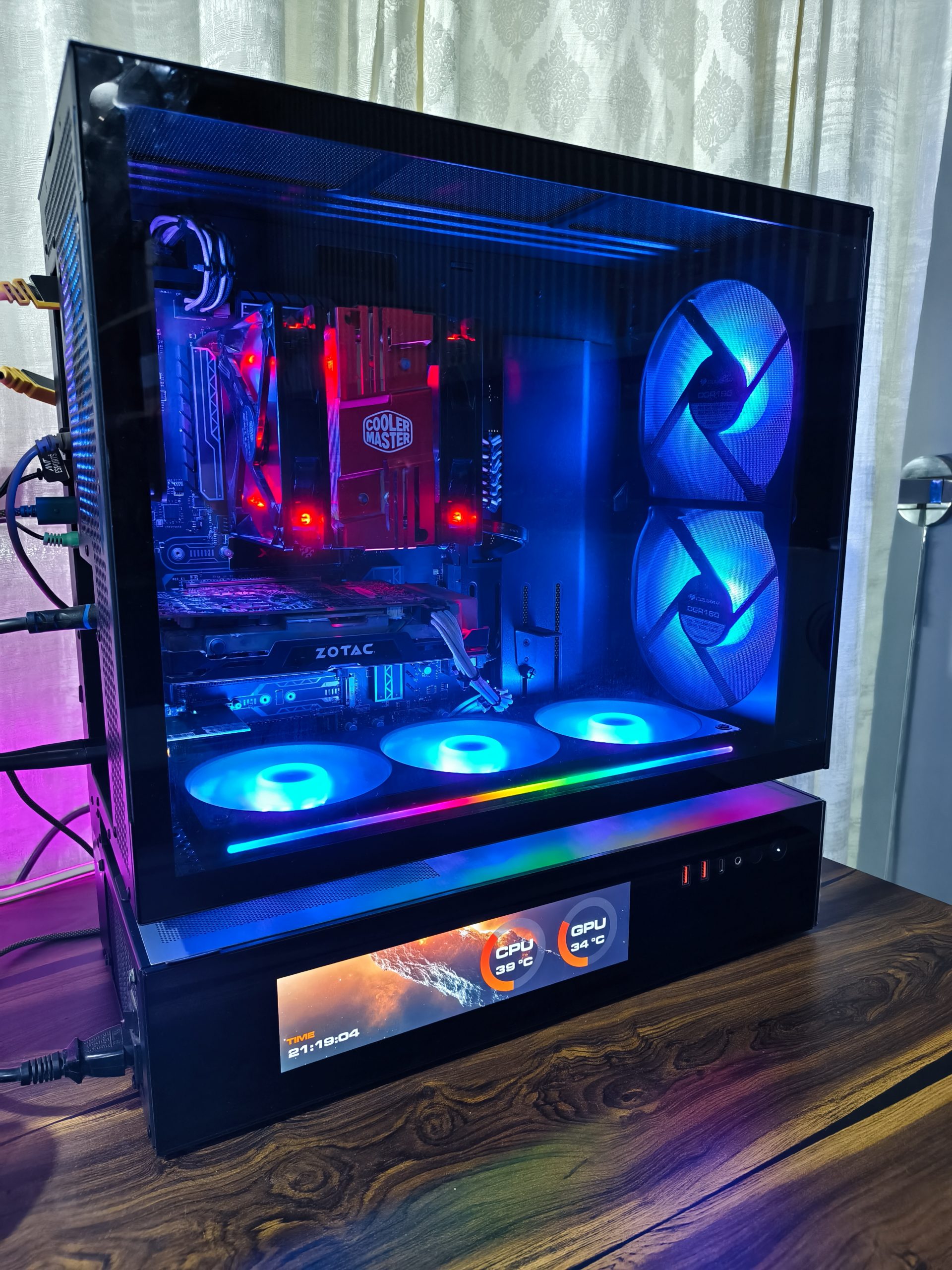 Ένας υπολογιστής με διαφανές πλαϊνό πλαίσιο εμφανίζει ένα εξάρτημα Cooler Master, μια κάρτα γραφικών Zotac, φωτισμό RGB και μια οθόνη με ένδειξη «CPU 39°C» και «GPU 34°C».