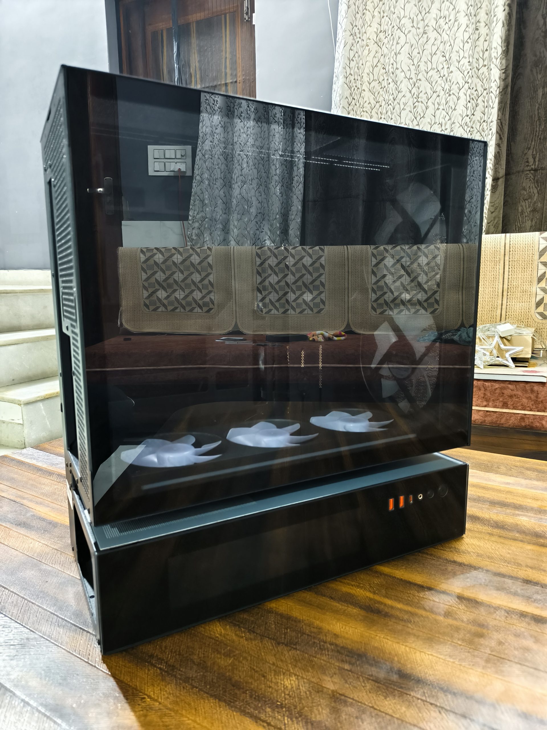 Μια μαύρη θήκη υπολογιστή χωρίς επωνυμία με ένα διαφανές πλαϊνό πάνελ που αποκαλύπτει τρεις εσωτερικούς ανεμιστήρες, τοποθετημένες σε ξύλινο πάτωμα.