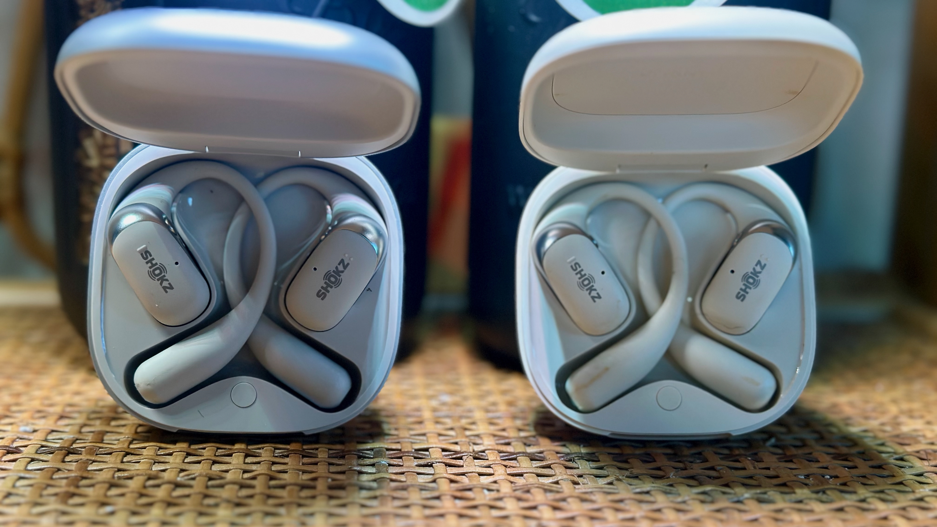 Οι θήκες Shokz OpenFit 2 Plus (αριστερά) και OpenFit 2 (δεξιά) είναι ανοιχτές και υπό γωνία, ώστε τα ακουστικά φόρτισης να είναι ορατά. Και τα δύο φαίνονται πανομοιότυπα, εκτός από το ότι το 2+ είναι ασημί και το 2 είναι λευκό.