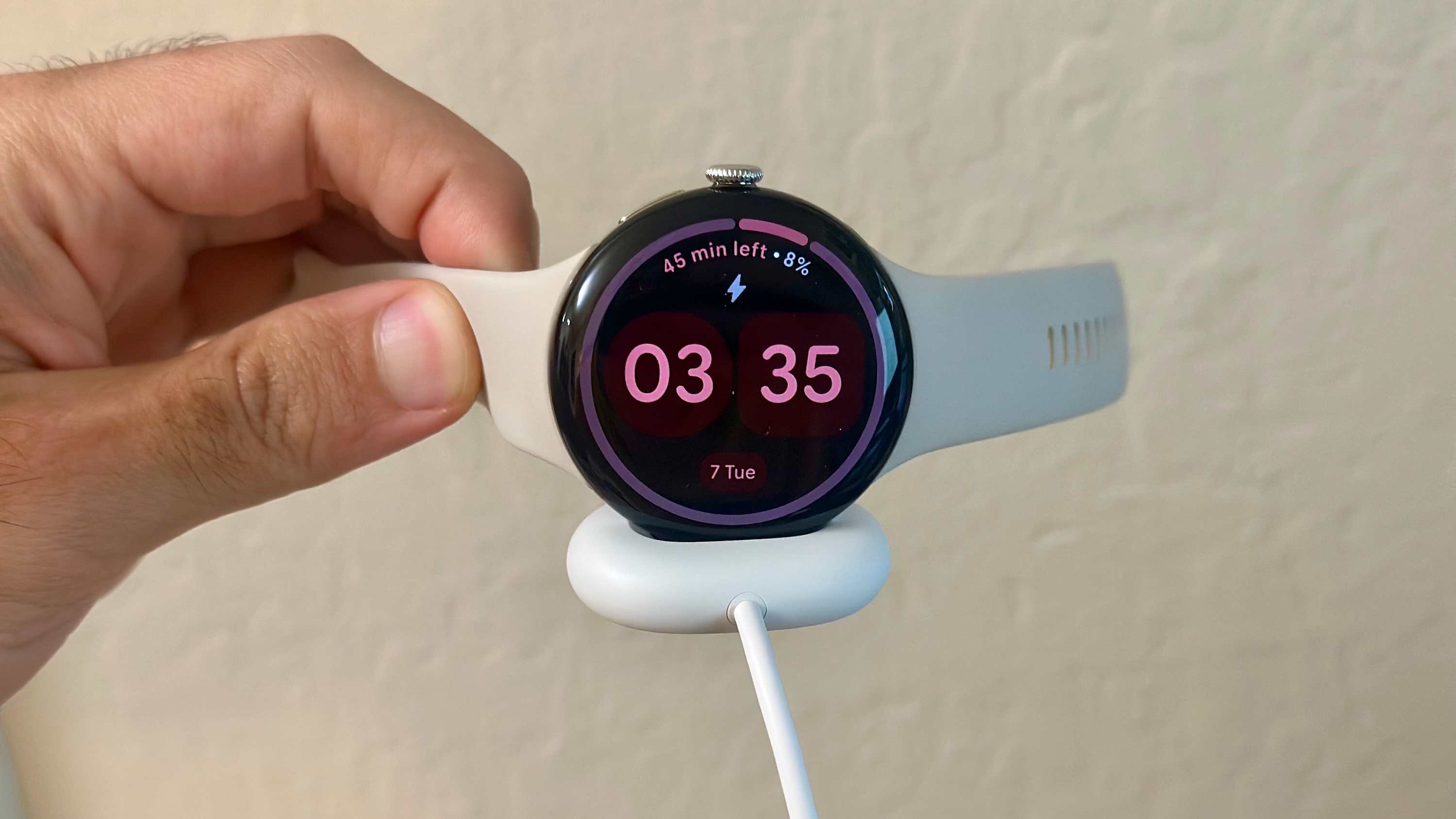 The Google Pixel Watch 4 held in hand with the Quick Charge Dock magnetically attached to the bottom.