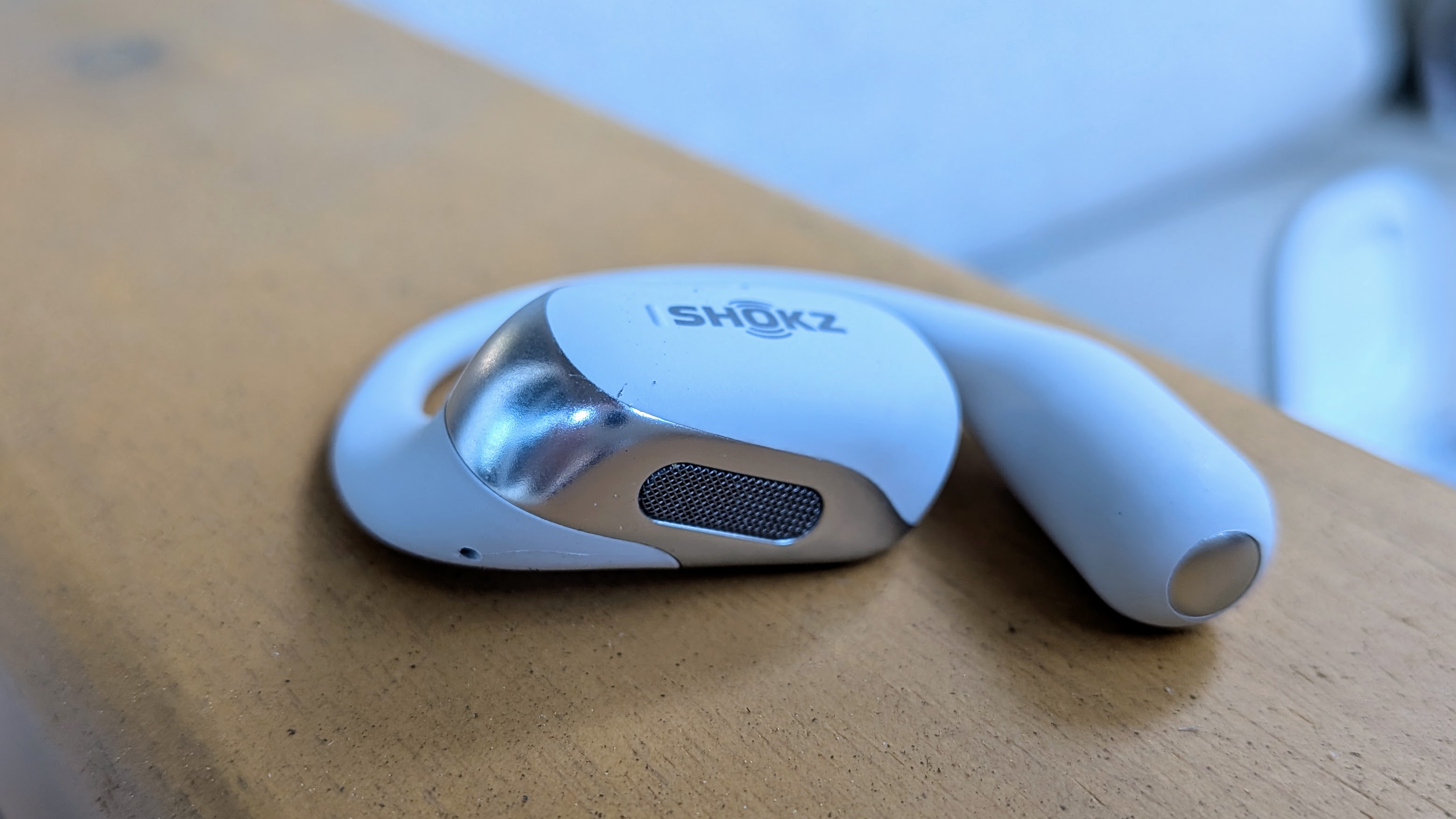Κοντινό πλάνο ενός μεμονωμένου ακουστικού Shokz OpenFit 2+, εστιασμένο στη σχάρα των ηχείων στο κάτω μέρος που γέρνει προς το αυτί σας.