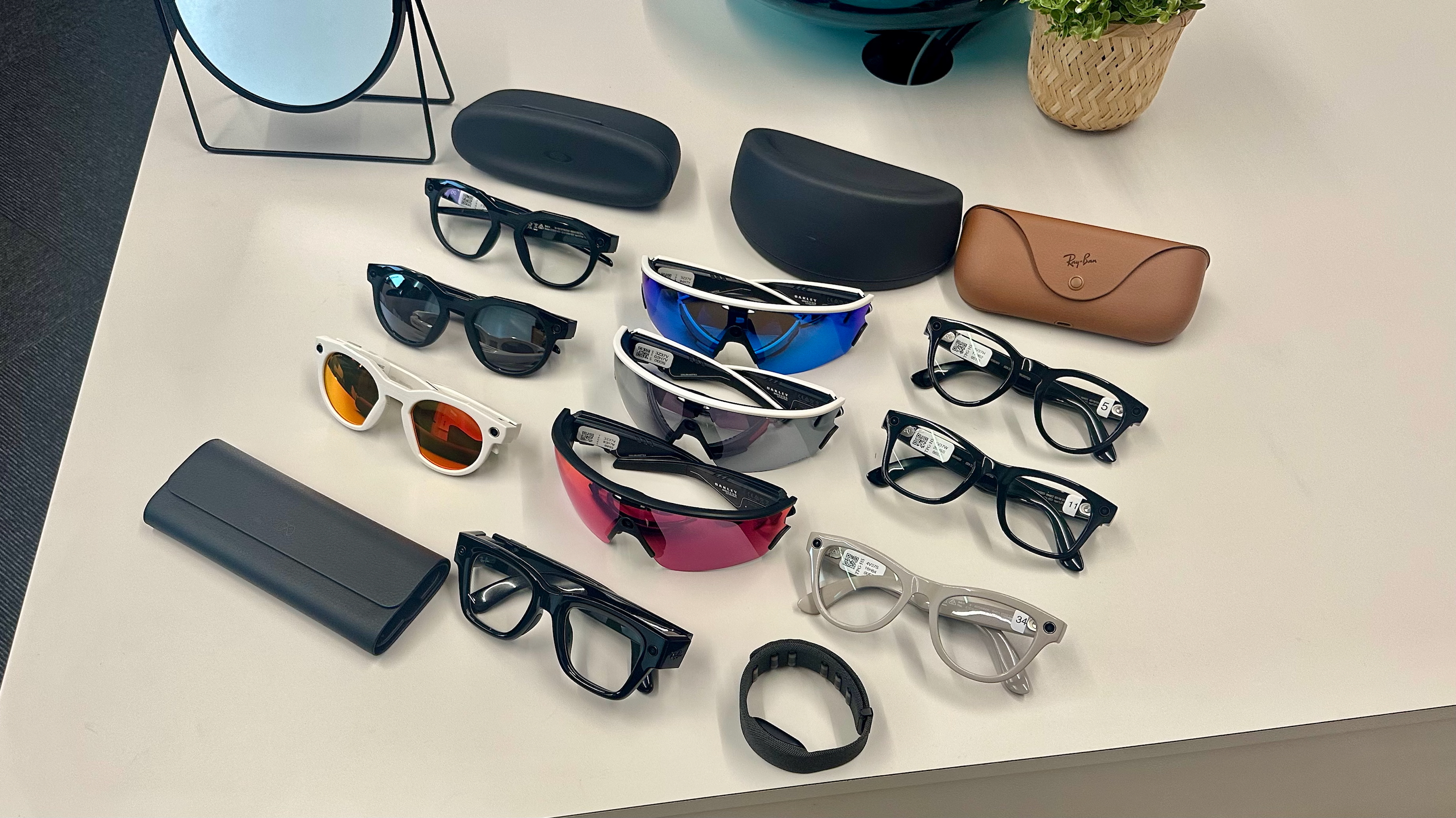 Τρία Oakley Meta HSTN, τρία Oakley Meta Vanguard και τρία Ray-Ban Meta (Gen 2), μαζί με θήκες, που κάθονται πάνω από ένα τραπέζι σε διάφορα στυλ, μαζί με τα γυαλιά Meta Ray-Ban Display μπροστά τους.