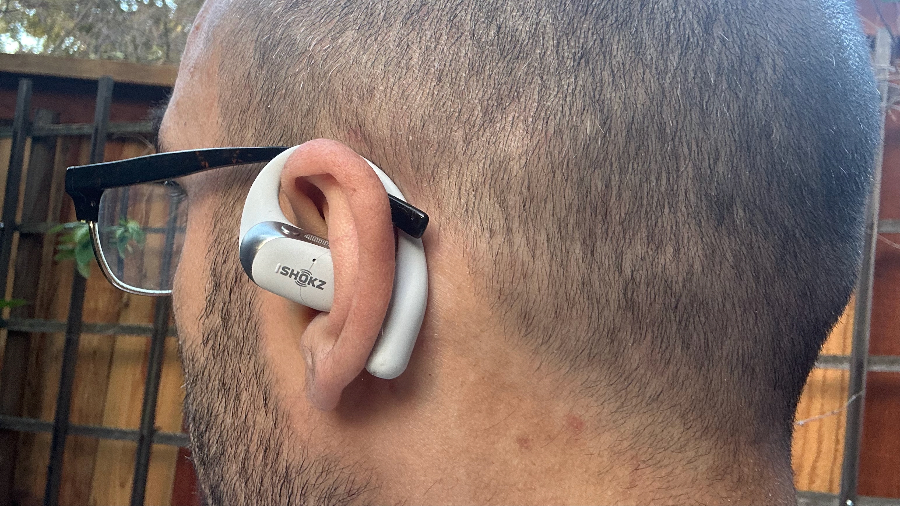 Μια αυτοφωτογραφία του συγγραφέα που φοράει ένα ακουστικό Shokz OpenFit 2 Plus στο αριστερό του αυτί, με γωνία ώστε να δείχνει το άγκιστρο πίσω από το αυτί του να ταιριάζει δίπλα στο μπράτσο των γυαλιών του.