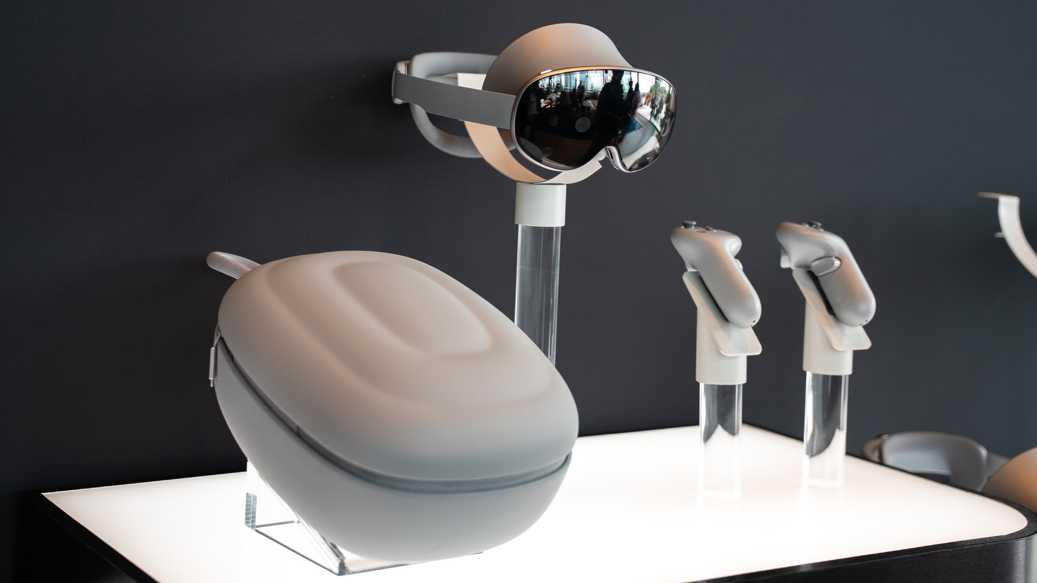 Τα ακουστικά Samsung Galaxy XR, η θήκη μεταφοράς και τα χειριστήρια σε τέσσερα βάθρα πάνω από μια λευκή, φωτισμένη επιφάνεια.