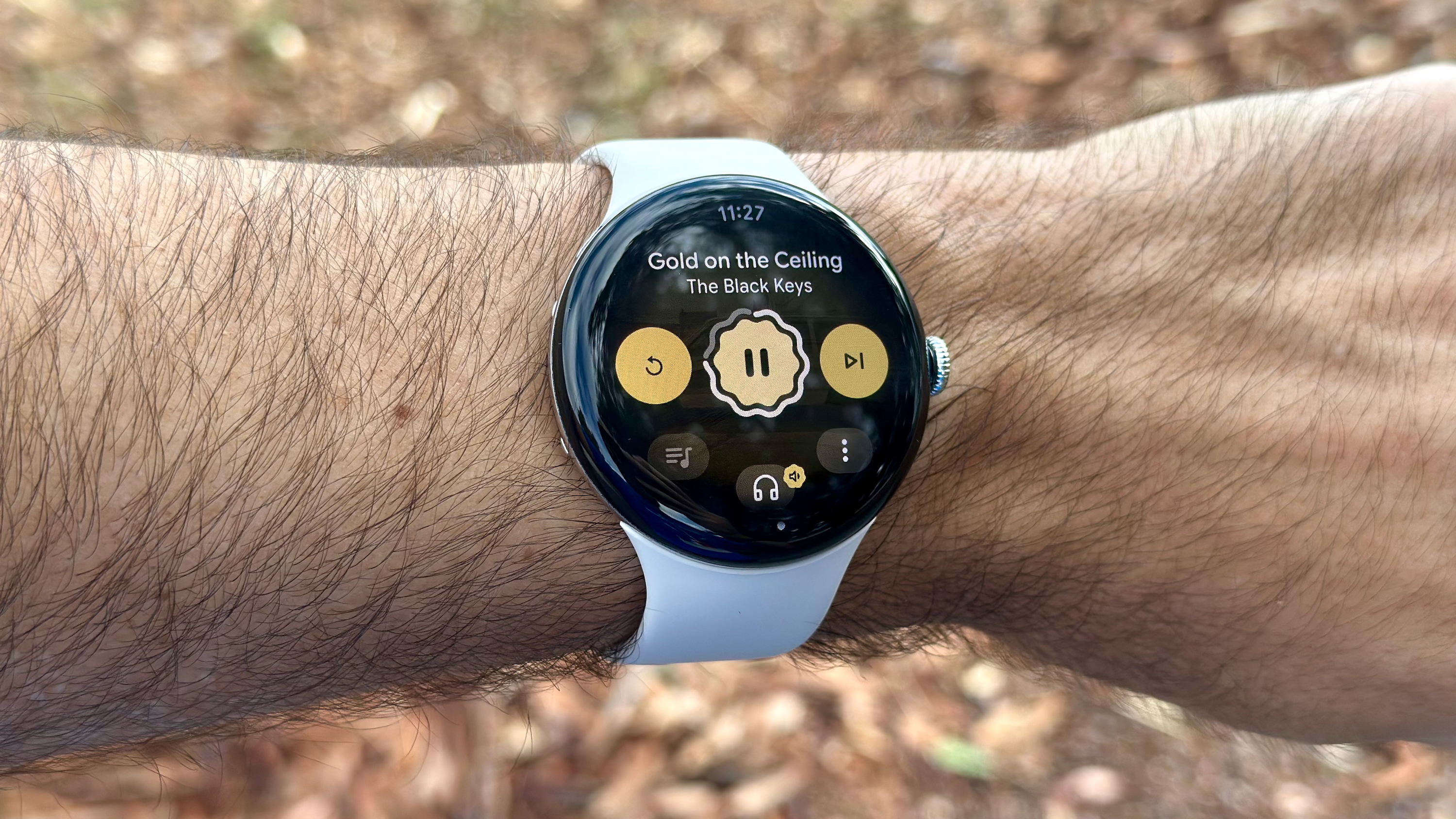 Μια φωτογραφία του Google Pixel Watch 4 σε έναν καρπό σε εξωτερικό χώρο, που δείχνει τα στοιχεία ελέγχου αναπαραγωγής μουσικής για μια λίστα αναπαραγωγής Pandora.