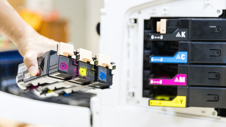 Ένα άτομο που κρατά δοχεία μελάνης εκτυπωτή δίπλα σε έναν εκτυπωτή.