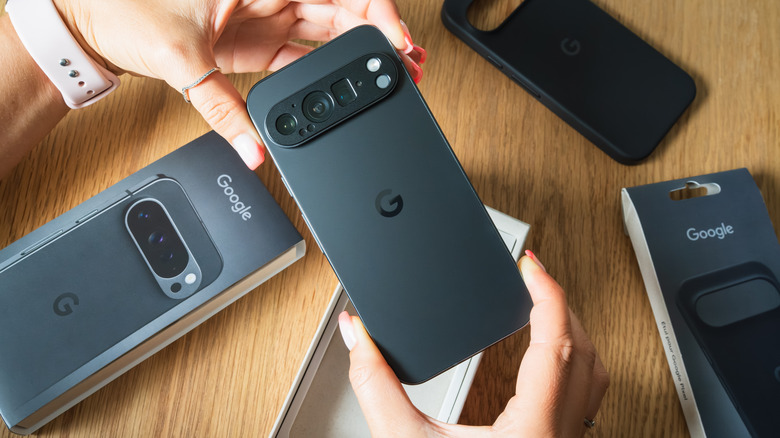 Ένα ζευγάρι χέρια κρατούν ένα νέο τηλέφωνο Google Pixel αμέσως μετά την αποσυσκευασία του πάνω από ένα ξύλινο τραπέζι.