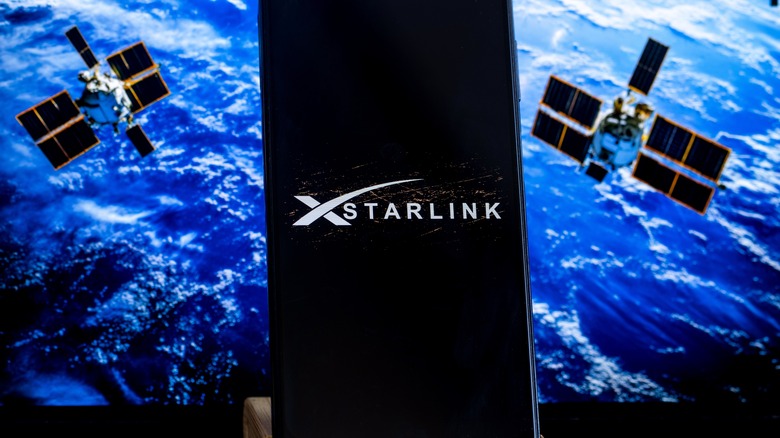 Το λογότυπο Starlink σε ένα tablet, σε φόντο δορυφόρων σε τροχιά γύρω από τη Γη.