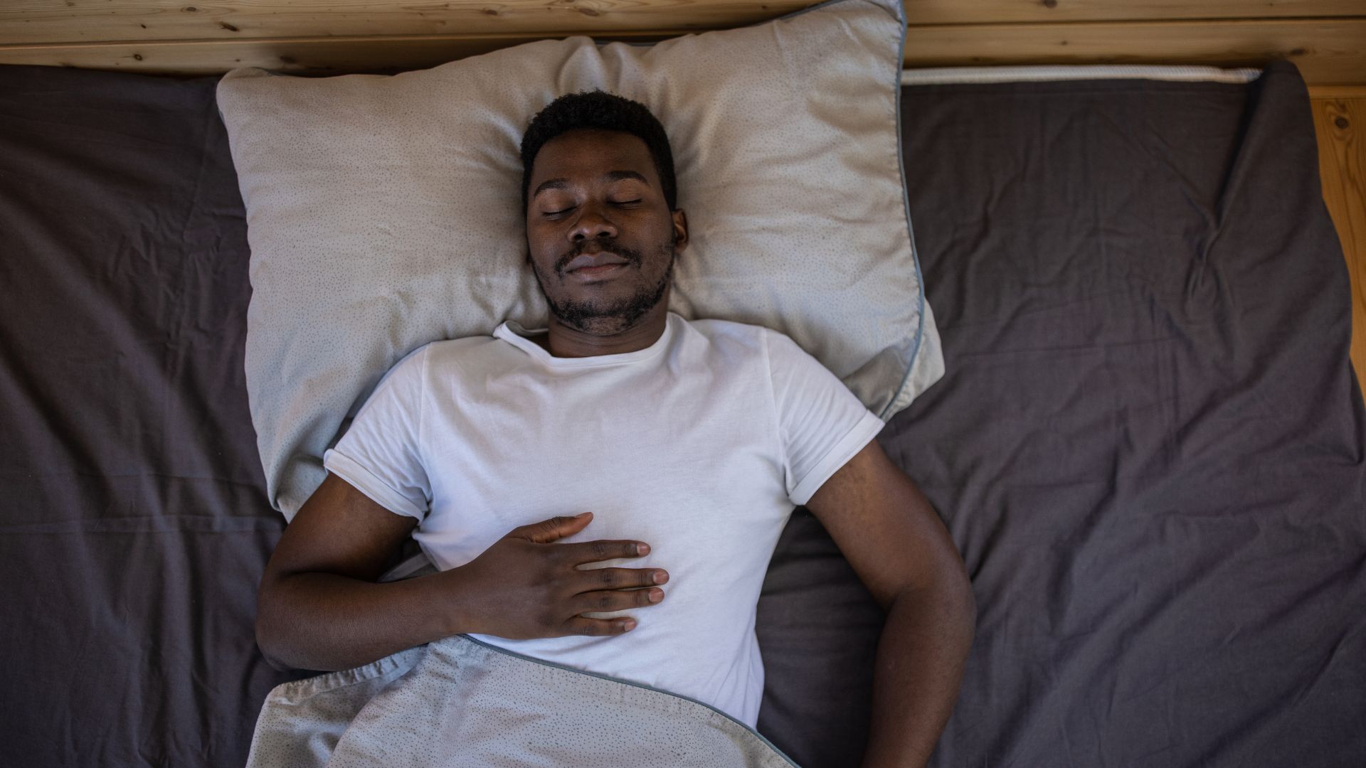 Αν δεν κοιμάστε καλά, η άσκηση δεν αρκεί! Η νέα έρευνα αποκαλύπτει το μυστικό για optimal υγεία! Ένας άντρας είναι ξαπλωμένος ανάσκελα στο κρεβάτι με τα μάτια κλειστά και το ένα χέρι ακουμπισμένο στο στήθος του.