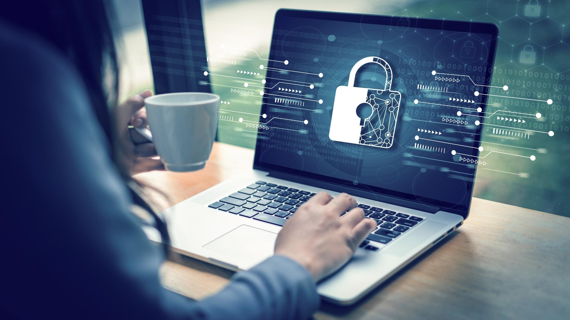 Μια γυναίκα που χρησιμοποιεί το laptop της με ασφάλεια με ένα φλιτζάνι καφέ στο χέρι