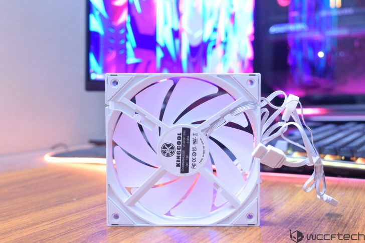 Ένας λευκός ανεμιστήρας KINGCOOL DC12V με αριθμό μοντέλου AV12025H12SU εμφανίζεται σε ένα ξύλινο τραπέζι, με μια πολύχρωμη οθόνη υπολογιστή στο φόντο.