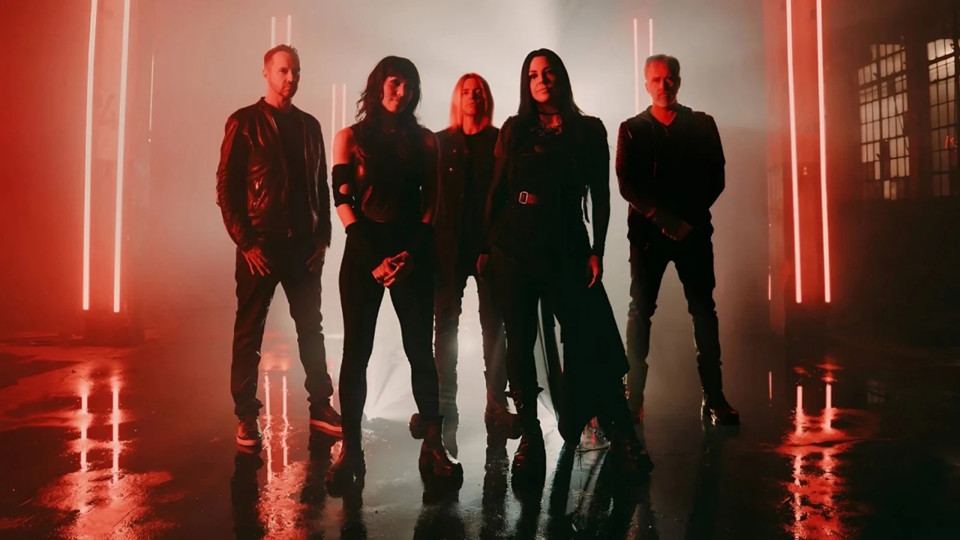 Μια ομάδα πέντε ατόμων στέκεται σε ένα αμυδρά φωτισμένο δωμάτιο με κόκκινο χρώμα με ανακλαστικά δάπεδα και κάθετες φωτεινές ράβδους στο βάθος.