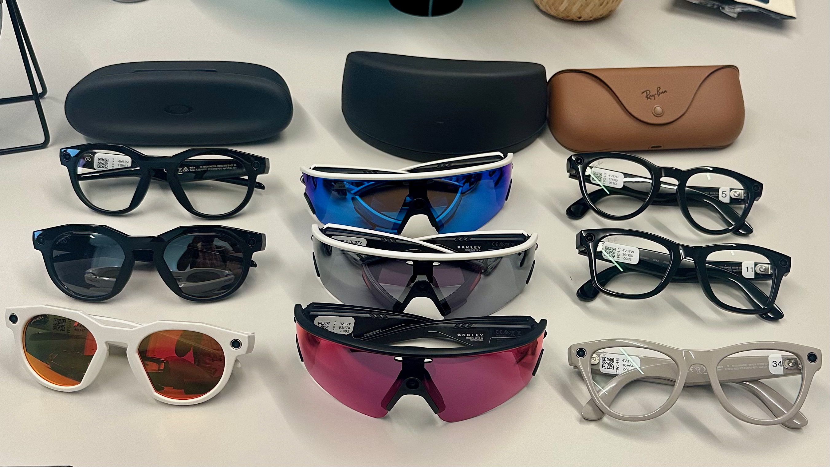 Τρεις Oakley Meta HSTN, τρεις Oakley Meta Vanguard και τρεις Ray-Ban Meta (Gen 2), μαζί με θήκες, που κάθονται πάνω σε ένα τραπέζι σε διάφορα στυλ.