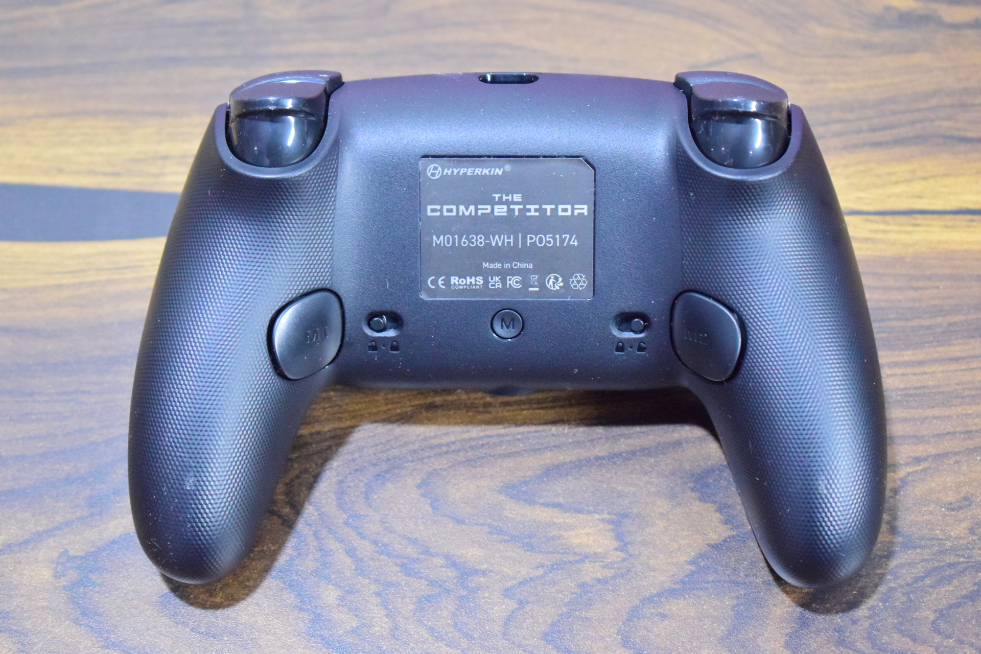 Ικανοποιητικός ελεγκτής προϋπολογισμού για PC και Xbox Η πίσω όψη ενός ελεγκτή Hyperkin The Competitor με αριθμό μοντέλου «M01638-WH» και «PO5174», που δείχνει διάφορα λογότυπα κανονισμών.