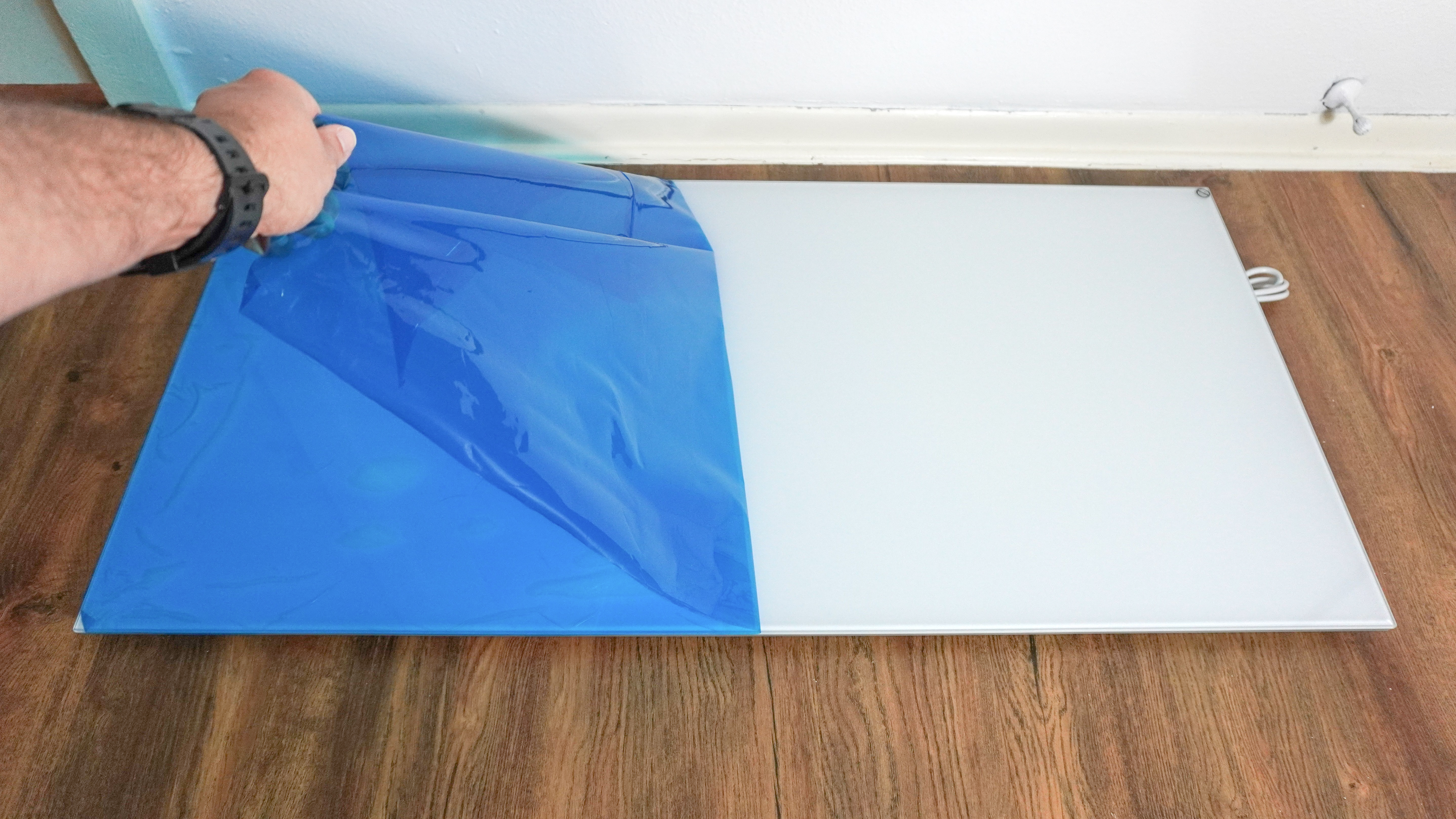 Ένα άτομο που ξεκολλάει την προστατευτική μεμβράνη που καλύπτει τον υπέρυθρο θερμαντήρα Boldr Kelvin για να αποκαλύψει την γυάλινη επιφάνεια του από κάτω