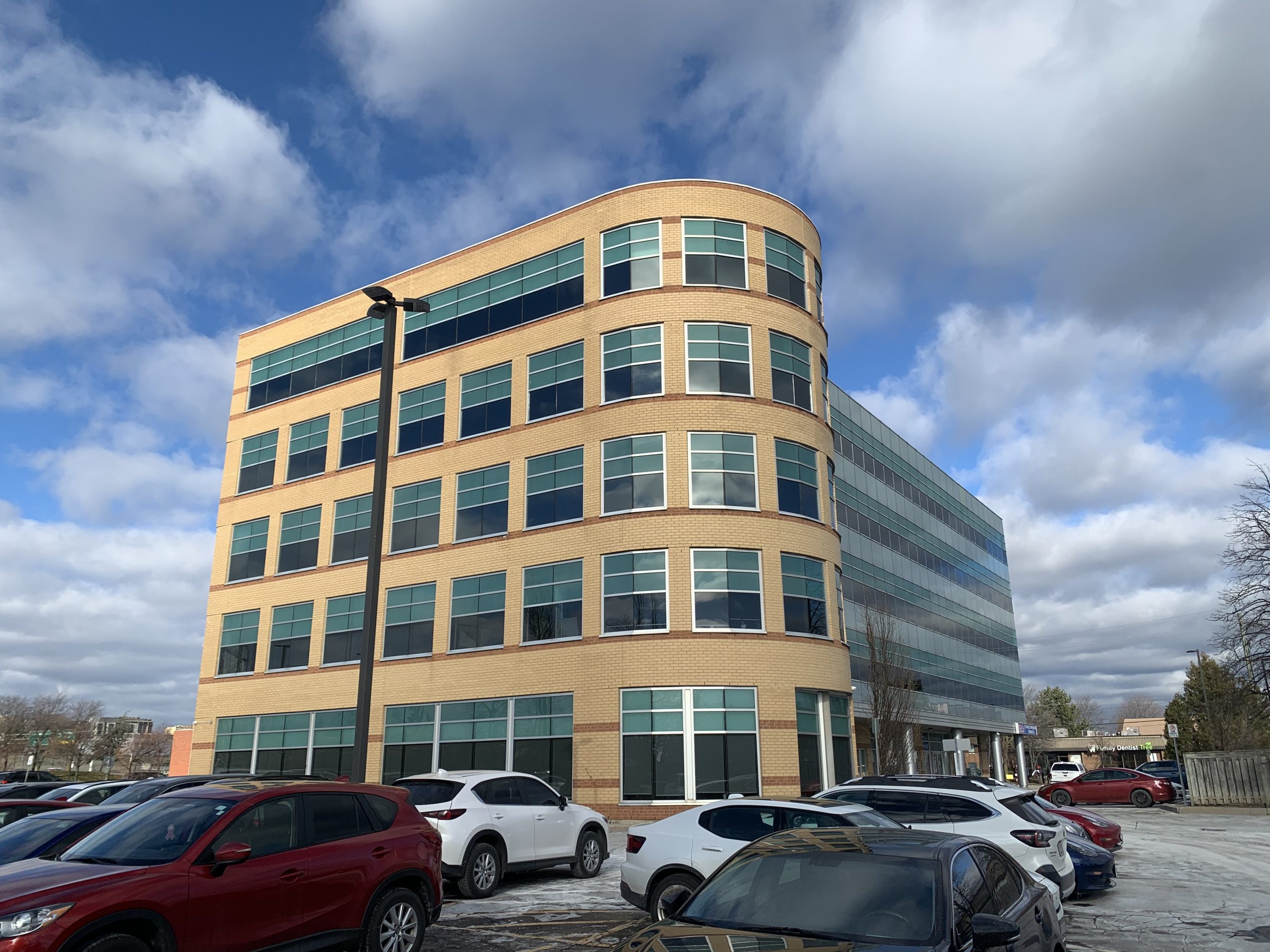 CWA Canada and Local Toronto Game Devs Protest at Rockstar Toronto in Solidarity with 34 Fired Workers A multi-story office building with a rounded corner design and modern glass windows, surrounded by a parking lot with several parked cars.