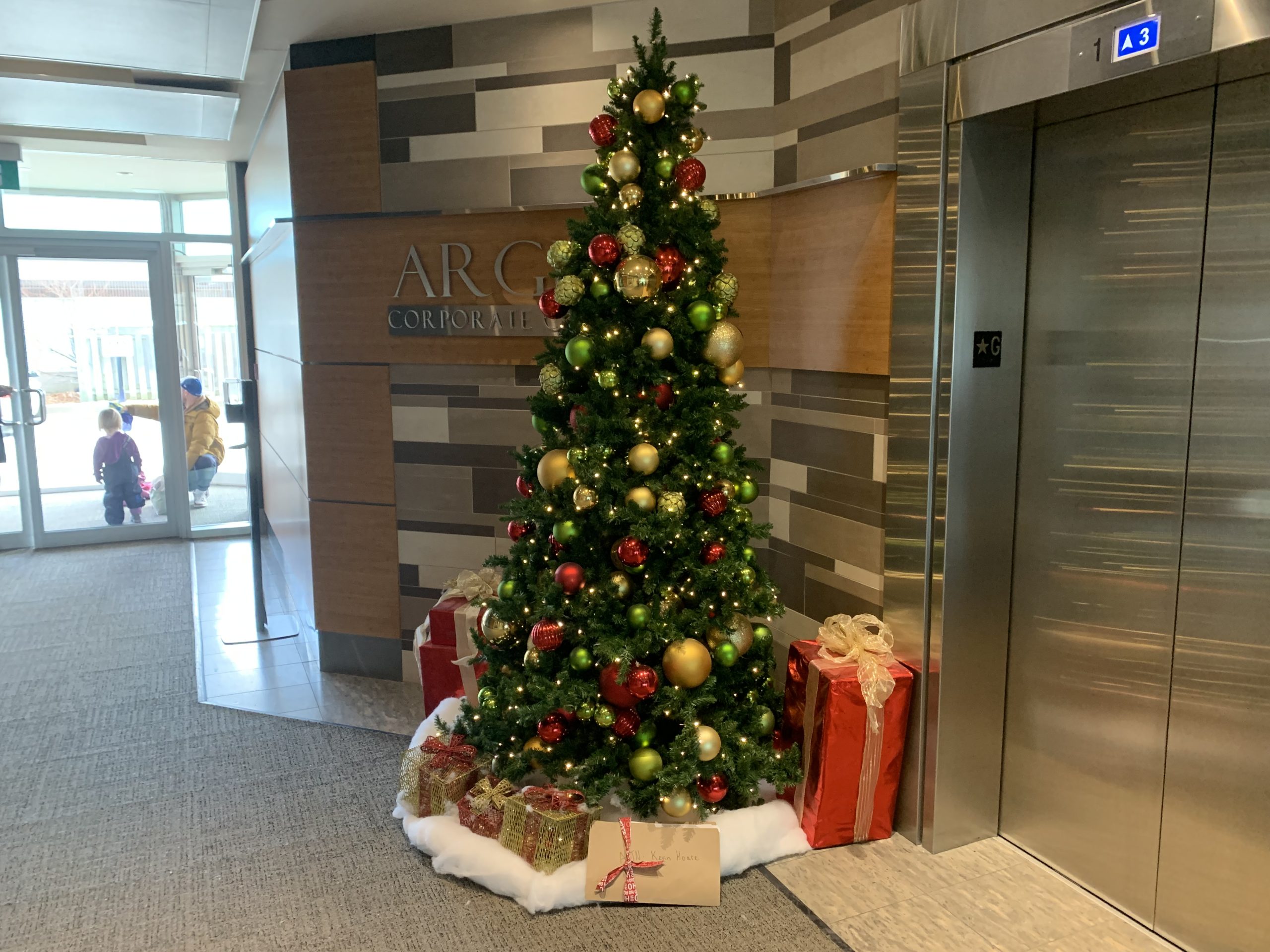 CWA Canada and Local Toronto Game Devs Protest at Rockstar Toronto in Solidarity with 34 Fired Workers A decorated Christmas tree with gifts underneath stands next to an elevator in a corporate lobby labeled 'ARC.'
