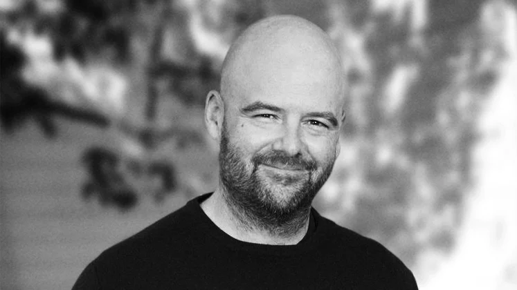 Dan Houser smiles at the camera in a black-and-white professional headshot