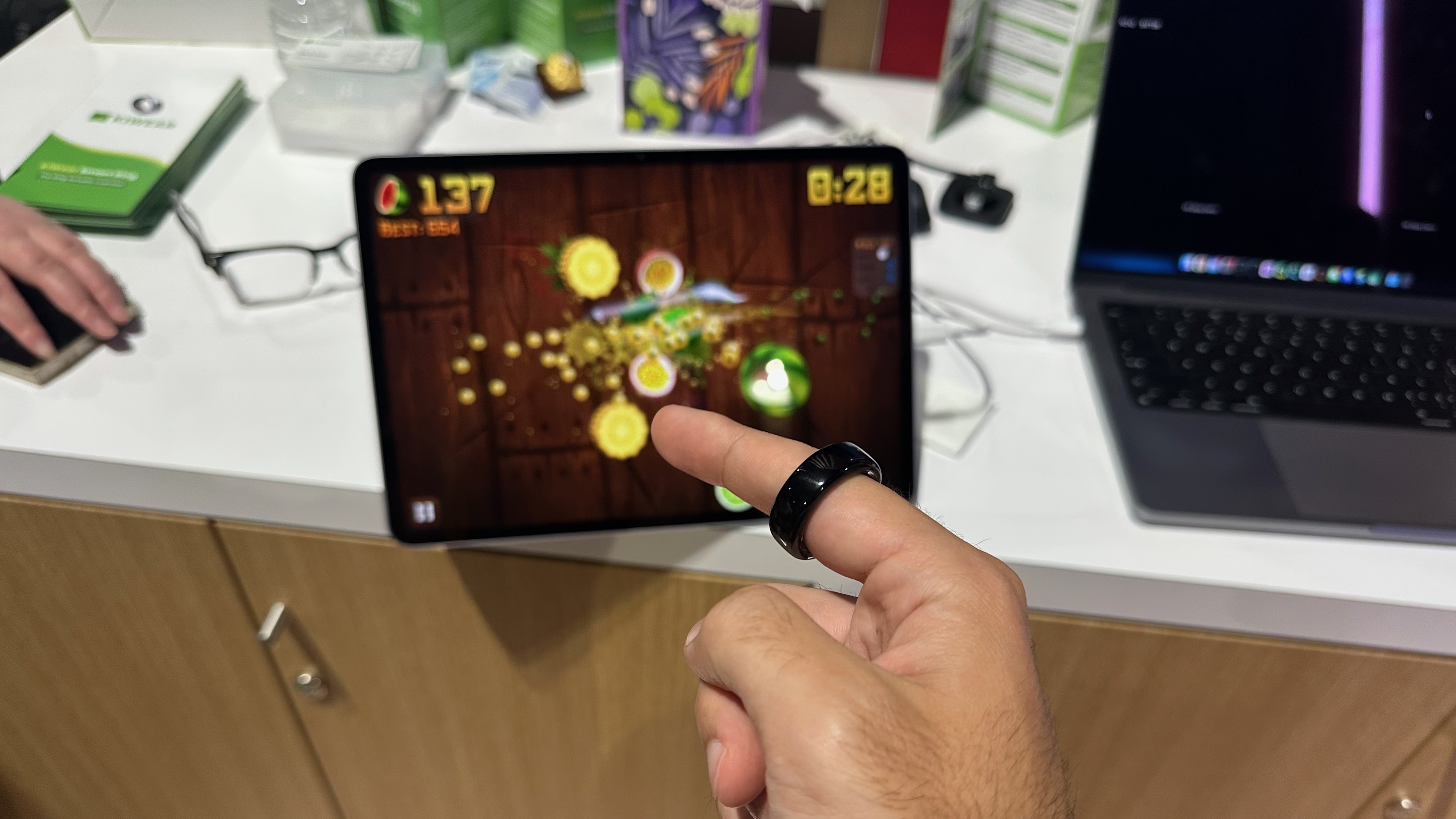 Ο συγγραφέας φοράει ένα έξυπνο δαχτυλίδι Kiwear ικανό να ελέγχει χειρονομίες, χρησιμοποιώντας το για να κόψει φρούτα σε Fruit Ninja σε ένα tablet.