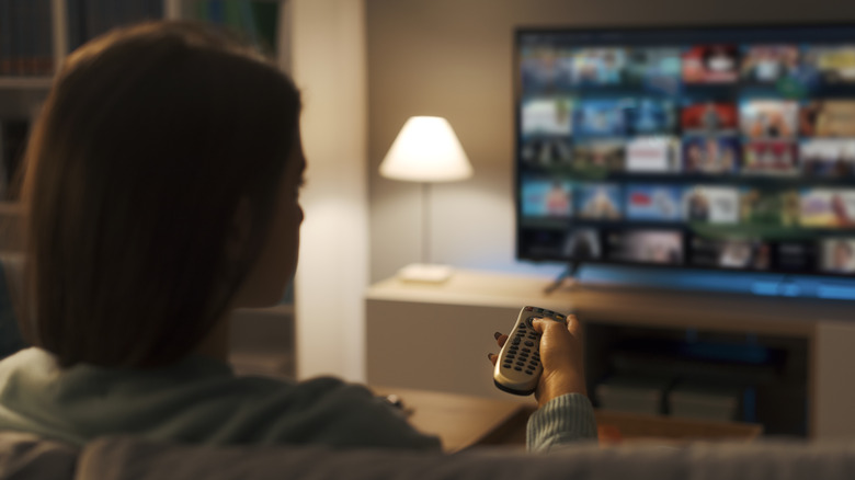 Γυναίκα κάθεται στον καναπέ και δείχνει το τηλεχειριστήριο στην τηλεόραση