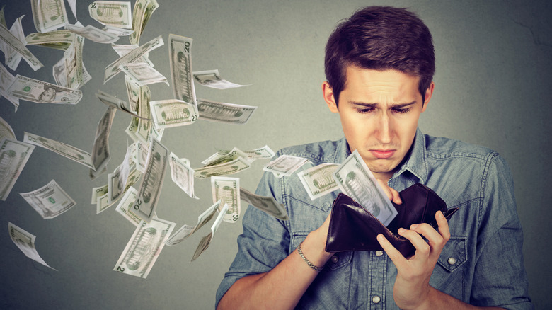 Ένας λυπημένος άνδρας που βλέπει τα χρήματα να πετούν από το πορτοφόλι του
