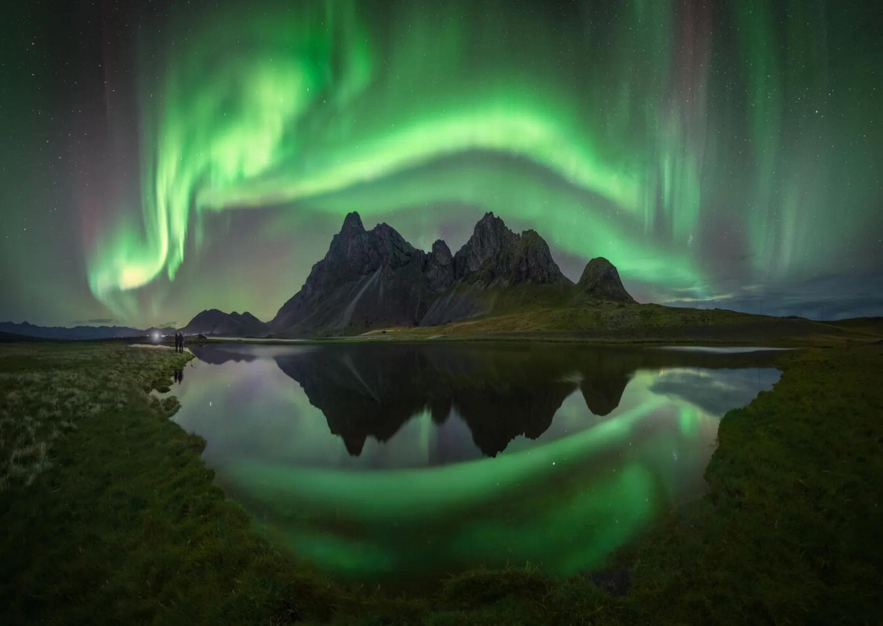 green aurora over mountains and reflected over water