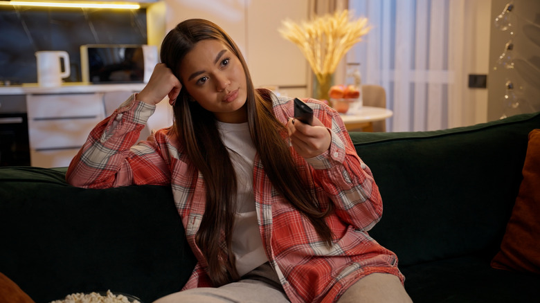 μια απογοητευμένη γυναίκα που βλέπει τηλεόραση στον καναπέ της