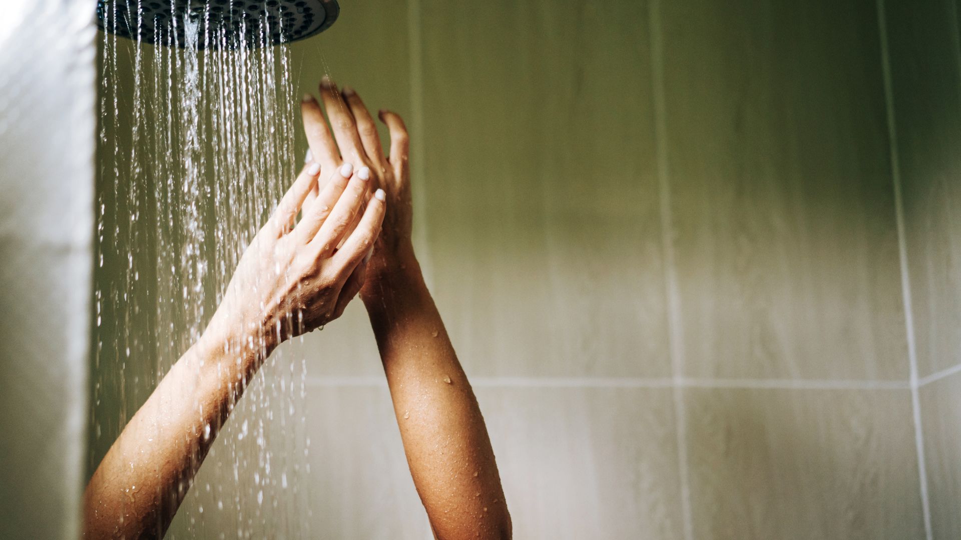 Ένα άτομο στέκεται σε ένα ντους με τα χέρια σηκωμένα. Το μπάνιο έχει επένδυση από ανοιχτόχρωμο ξύλο στον τοίχο.