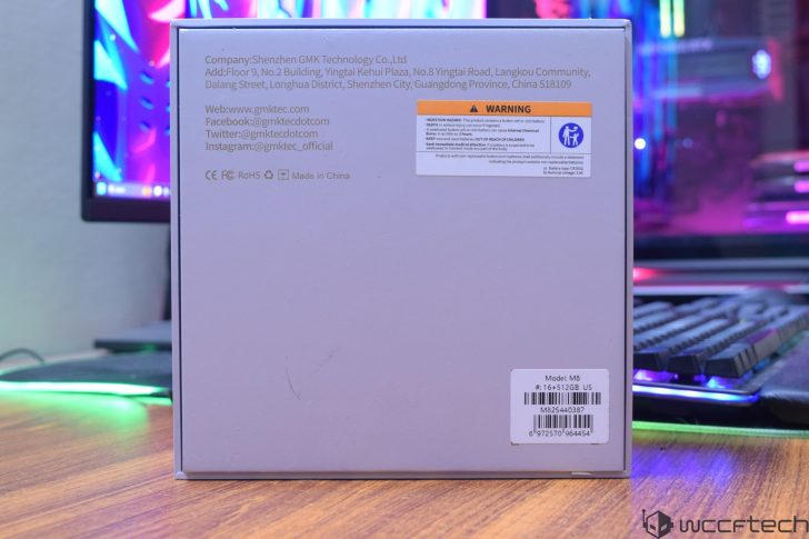 The image shows the back of a GMKtec M8 product box, displaying company contact information and a 'WARNING' label, with a model specification label indicating Model: M8, #: 16+512GB US.