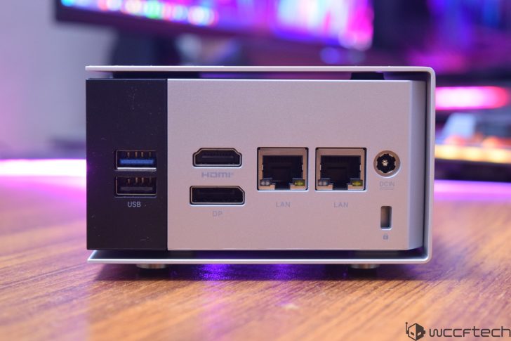 A mini PC with USB, HDMI, DP, LAN, and DC IN ports is situated on a wooden surface.