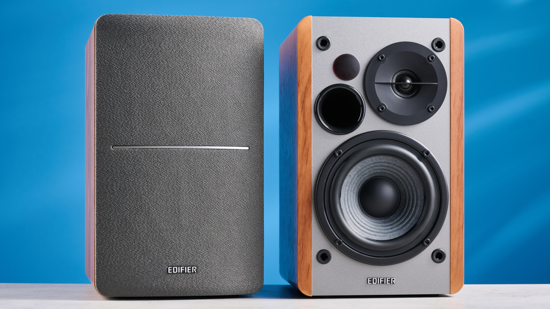 τα ηχεία βιβλιοθηκών edifier r1280t σε καφέ ξύλο φωτογραφισμένα στο μπλε φόντο, που δείχνουν τους επιλογείς ρύθμισης έντασης, τα εσωτερικά προγράμματα οδήγησης και τα τουίτερ, τις εισόδους RCA και aux και το τηλεχειριστήριο