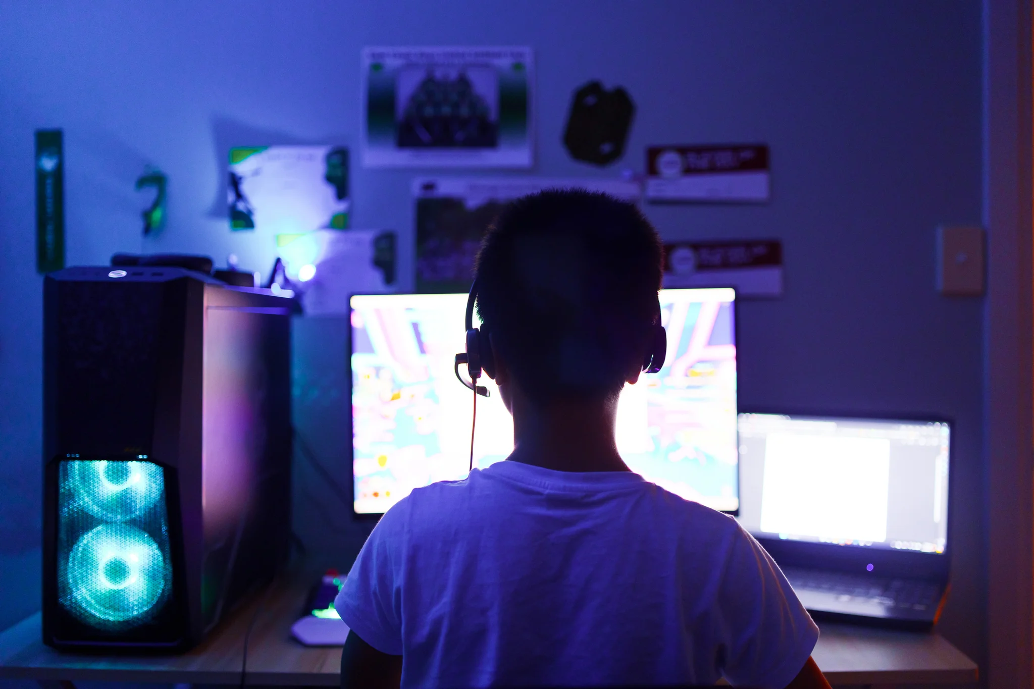 A child in a gaming headset using a gaming PC, viewed from behind