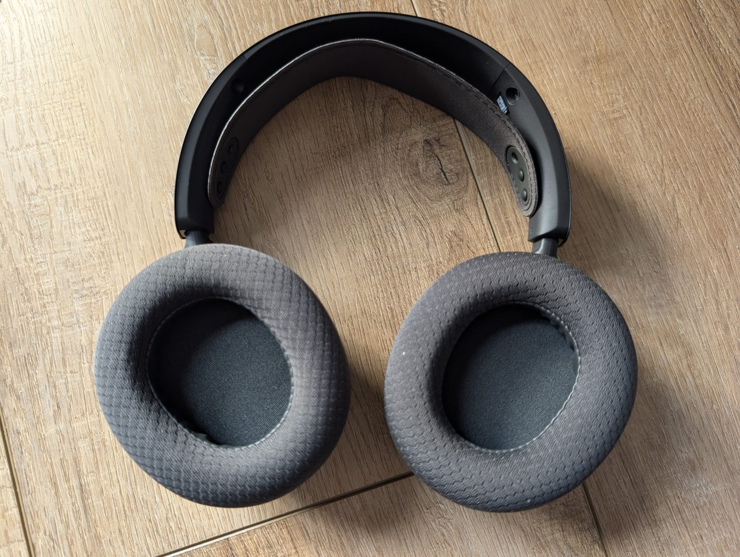 Ακουστικά πάνω από το αυτί χωρίς επωνυμία με γκρι υφασμάτινα μαξιλάρια αυτιών που στηρίζονται σε ξύλινη επιφάνεια.