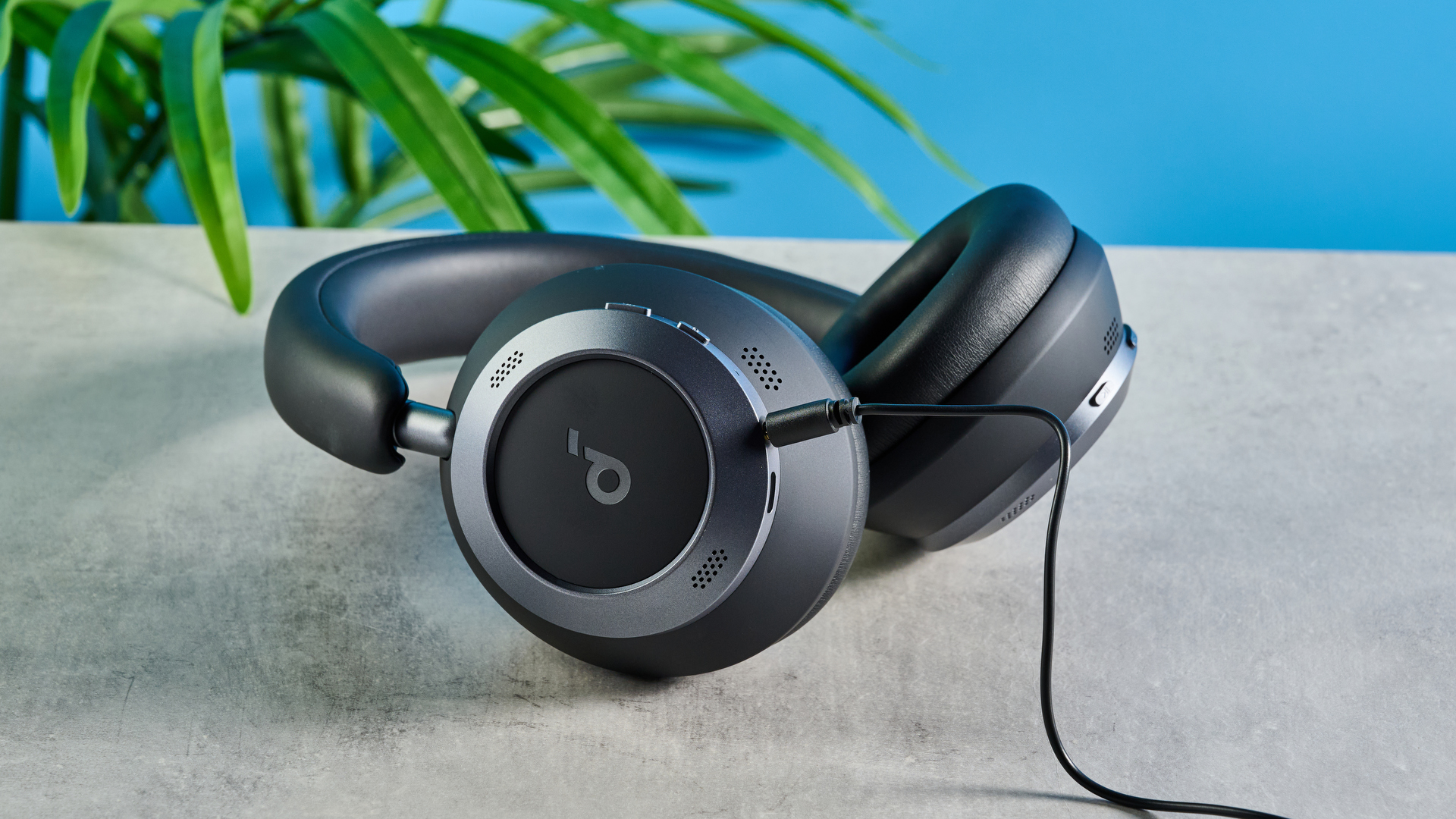 μια φωτογραφία ενός ζευγαριού μαύρων ακουστικών πάνω από το αυτί με μαλακά κύπελλα και ένα μαλακό κεφαλόδεσμο, φωτογραφημένη μπροστά σε μπλε φόντο