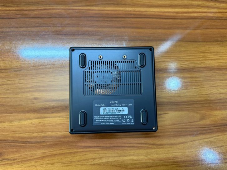 Η κάτω όψη ενός Minisforum mini PC μοντέλου NAB6, που δείχνει αεραγωγούς ψύξης και ετικέτες προϊόντων σε ξύλινη επιφάνεια.