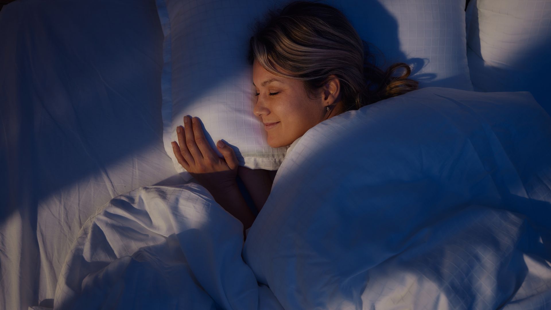 Μια γυναίκα που χαμογελά καθώς κοιμάται στο πλάι με το κεφάλι της ακουμπισμένο σε ένα μαξιλάρι.