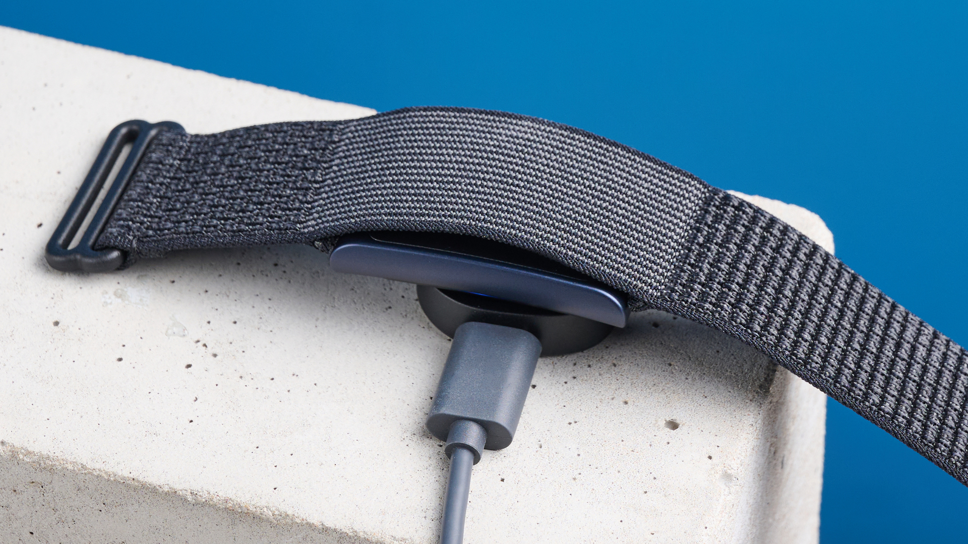 ο ιχνηλάτης γυμναστικής amazfit helio με σχέδιο χωρίς οθόνη, που δείχνει το γκρι λουράκι που φοριέται γύρω από τον καρπό και τον φορτιστή