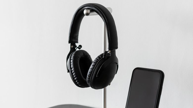 Ένα ακουστικό κρεμασμένο σε μια ασημένια βάση που φυλάσσεται δίπλα σε ένα smartphone