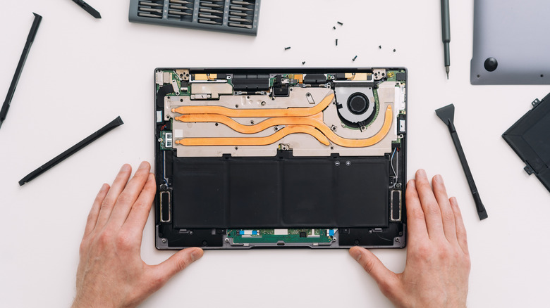 Ένα φορητό υπολογιστή που κάθεται σε ένα τραπέζι, άνοιξε, δείχνοντας ένα ζευγάρι χέρια έτοιμα να ξεκινήσουν μια επισκευή.