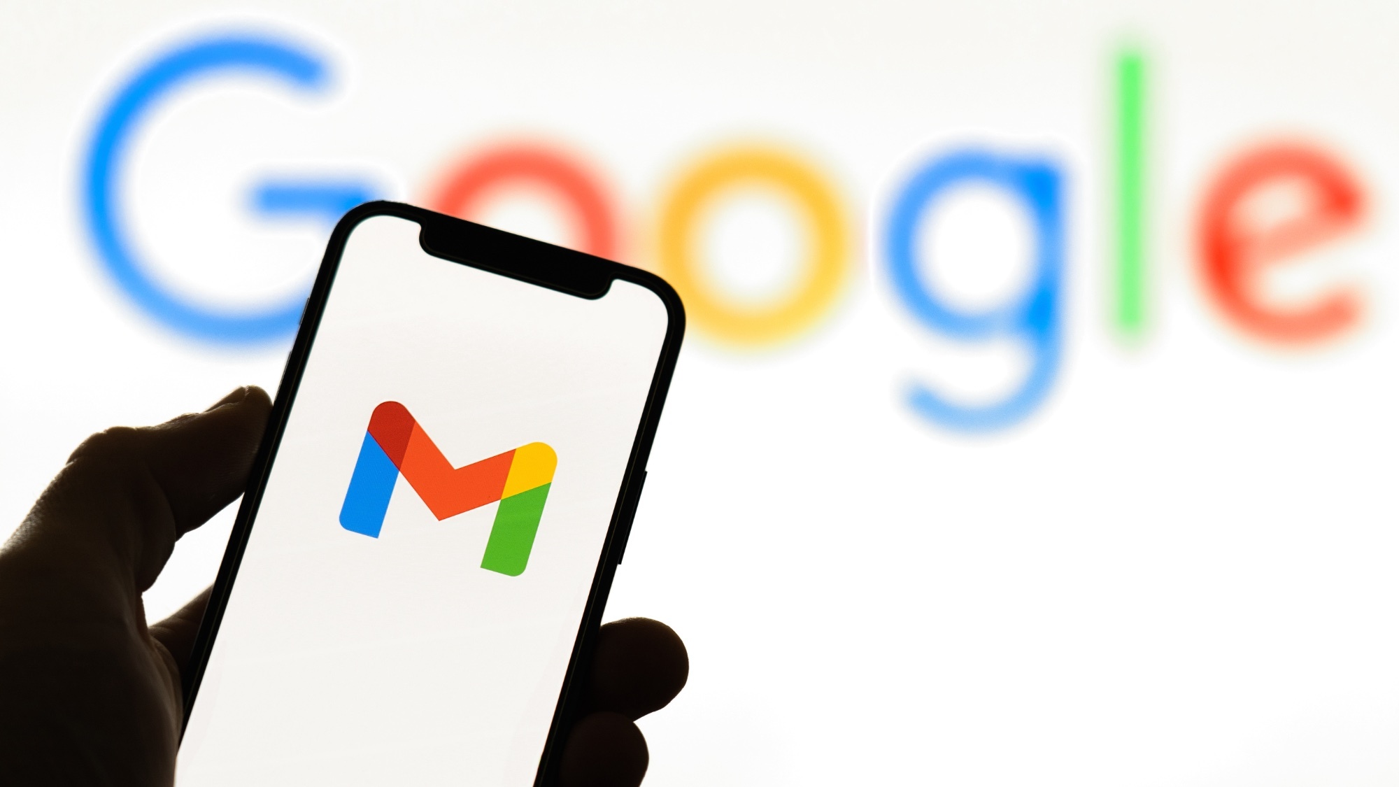 Ένα smartphone με το λογότυπο του Gmail, που κρατιέται από ένα χέρι, μπροστά σε φόντο της Google