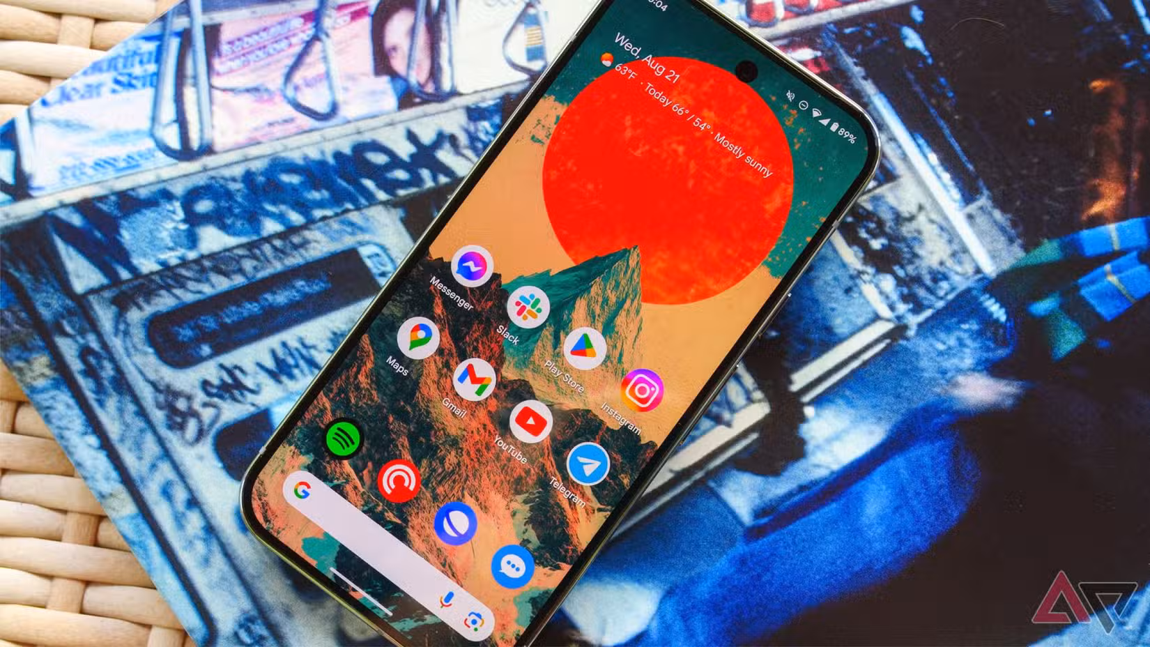 Το Pixel 9 Pro σε ένα ψάθινο τραπέζι και ξαπλωμένο πάνω από ένα μανίκι άλμπουμ με την οθόνη επάνω