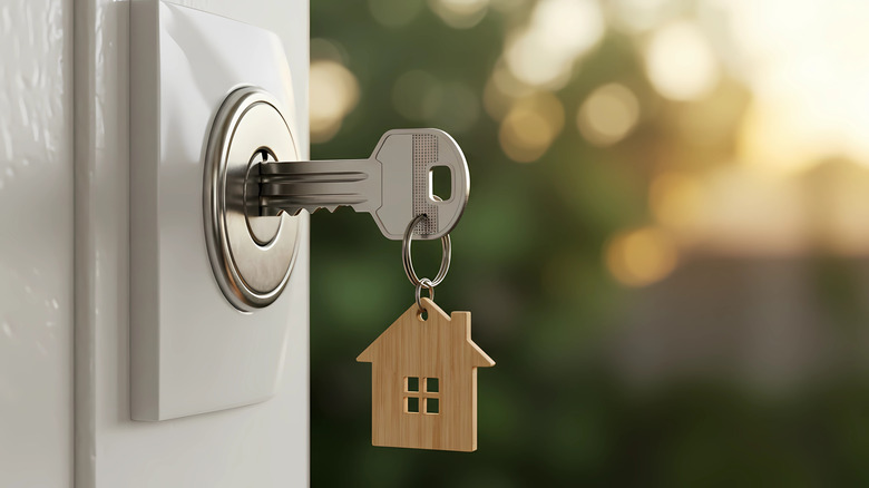 Ένα κλειδί με ένα στυλιζαρισμένο μπρελόκ για το σπίτι που εισάγεται στην κλειδαριά μιας ανοιχτής πόρτας.