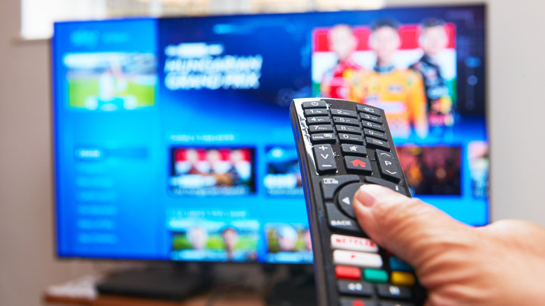 Τηλεχειριστήριο τηλεόρασης στο χέρι που στοχεύει σε ενεργοποιημένη τηλεόραση.