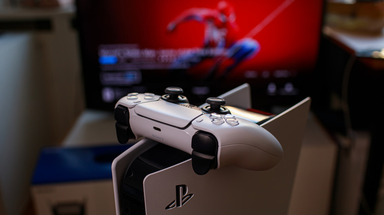 Ελεγκτής Dual Sense στην κονσόλα PlayStation 5 με τον Spider-Man στην οθόνη στο παρασκήνιο.