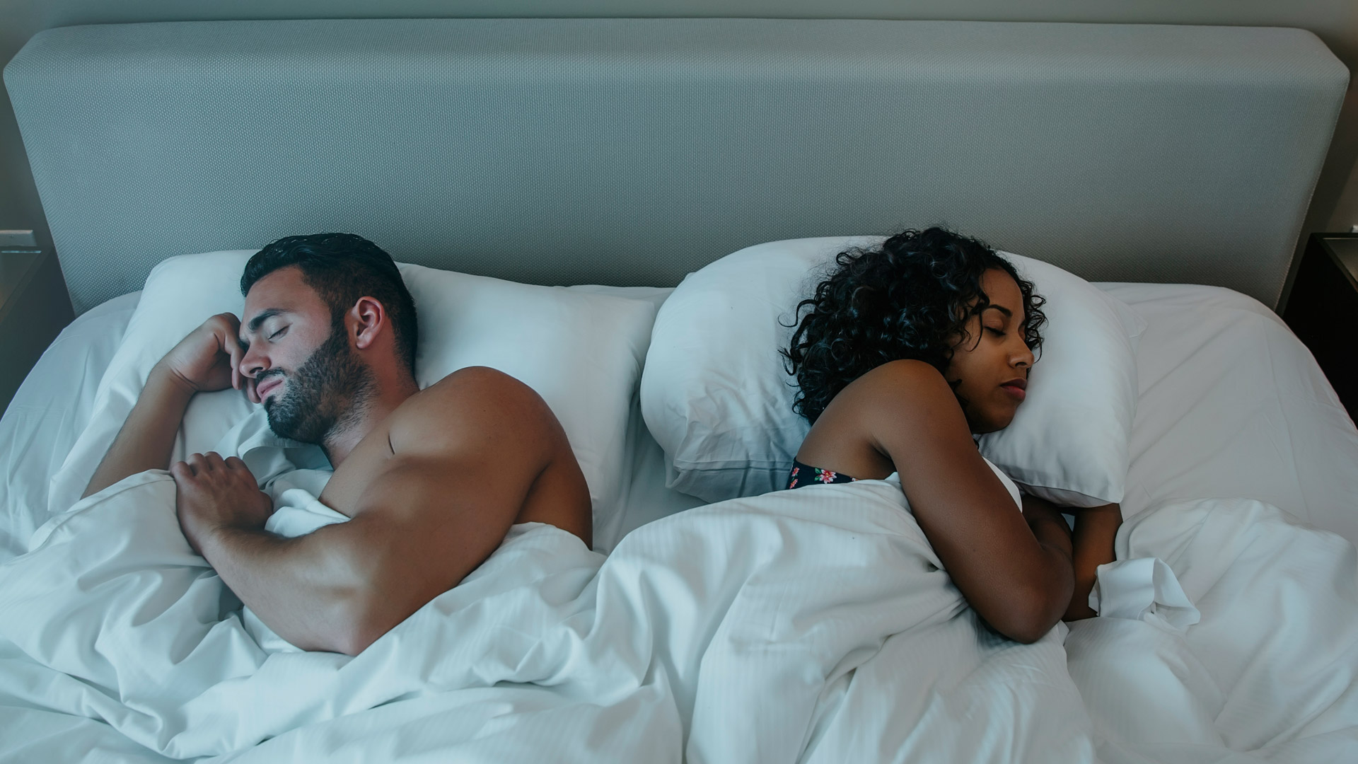 Ένα ζευγάρι κοιμάται στο κρεβάτι κάτω από λευκά σεντόνια, ξαπλωμένο πλάτη με πλάτη