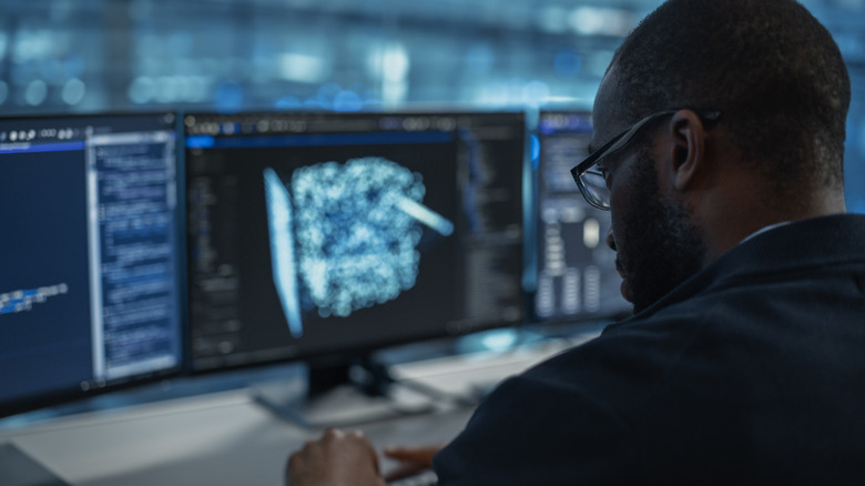 Άνθρωπος στο γραφείο που εκτελεί εργασίες υπολογιστή με τρεις οθόνες