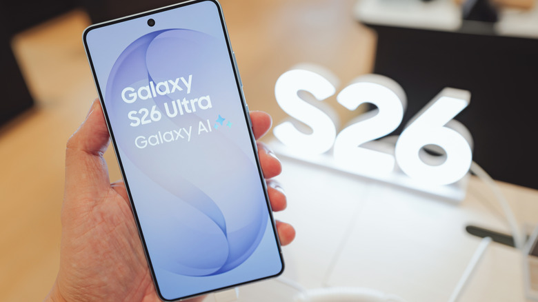 Ένα τηλέφωνο Samsung Galaxy S26 Ultra κρατιέται στο χέρι με ένα φως που μοιάζει με τις λέξεις S26 στο φόντο