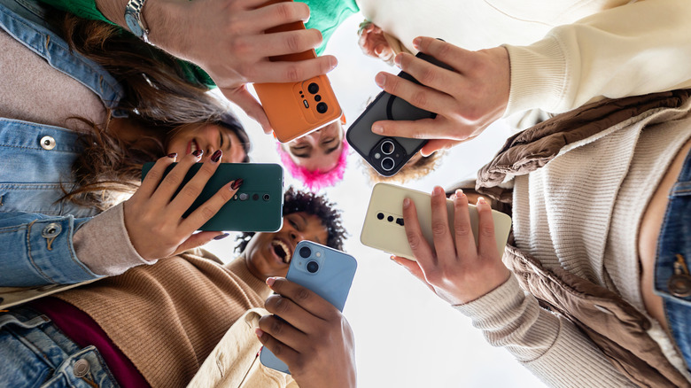 Μια ομάδα νέων ανθρώπων κοιτάζουν όλοι τα smartphone τους