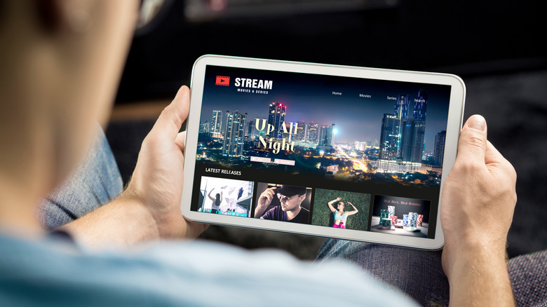 Ένας άντρας που κρατά ένα tablet που δείχνει μια υπηρεσία ροής ταινιών στην οθόνη